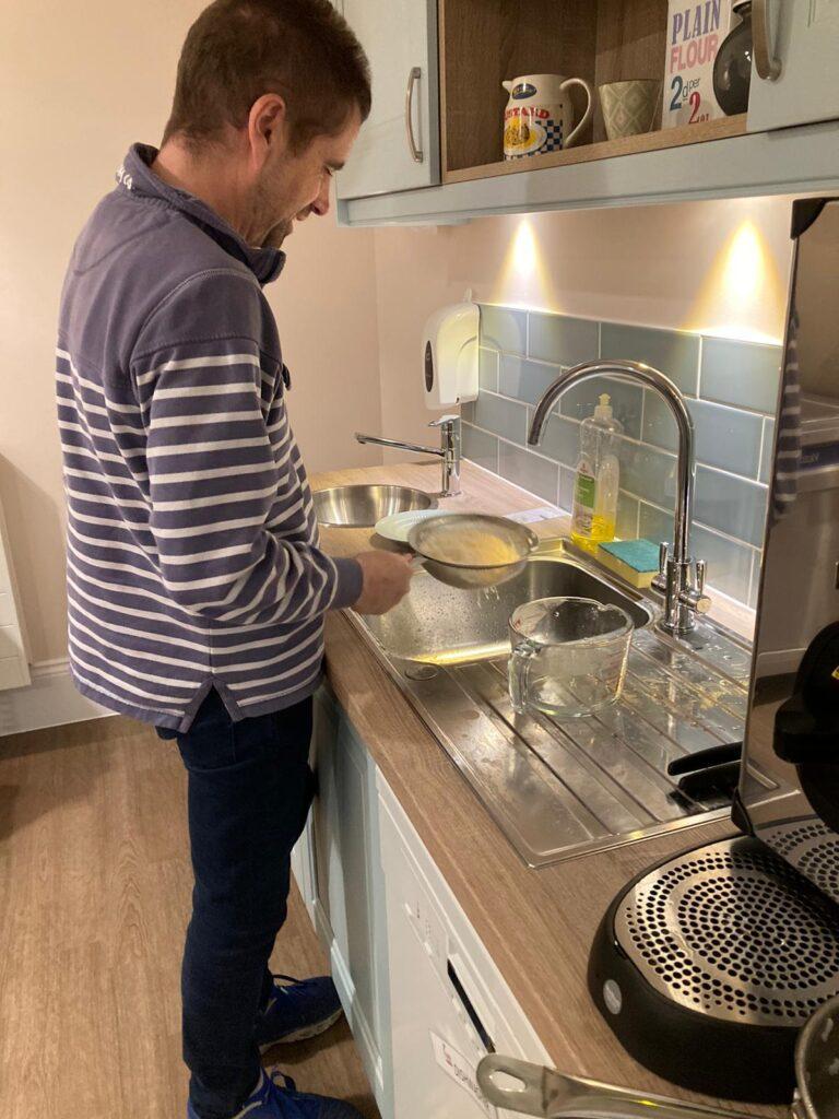 An inpatient with brain injuries standing at the sink washing rice as part of an occupational therapy goal