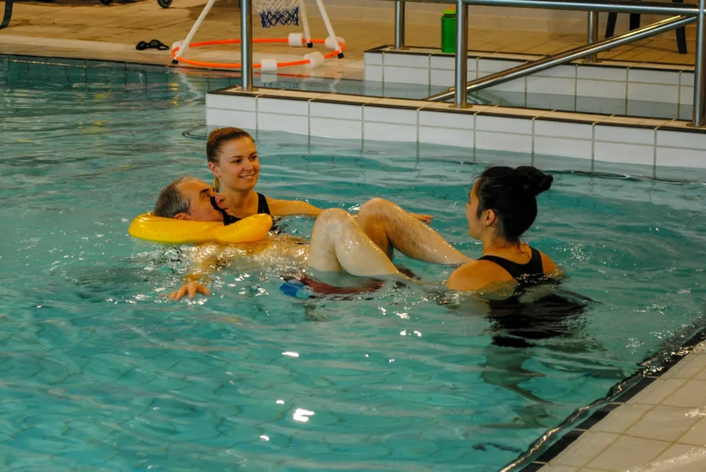 Rehab assistant and Physiotherapist in the hydro pool supporting patient floating using a float